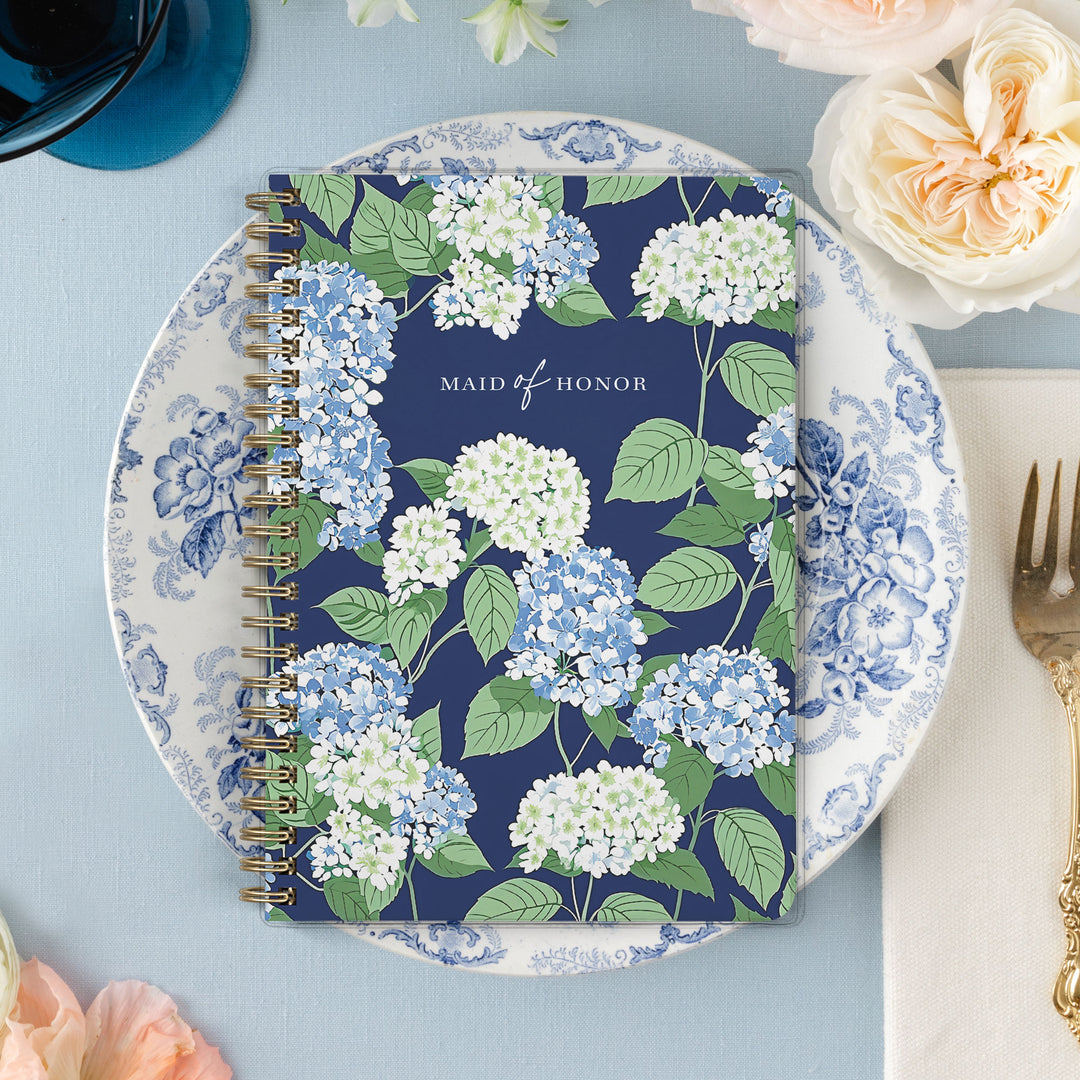 Our exclusive maid of honor planners are the perfect gift for your best friend, shown in a blue, white and green hydrangea pattern