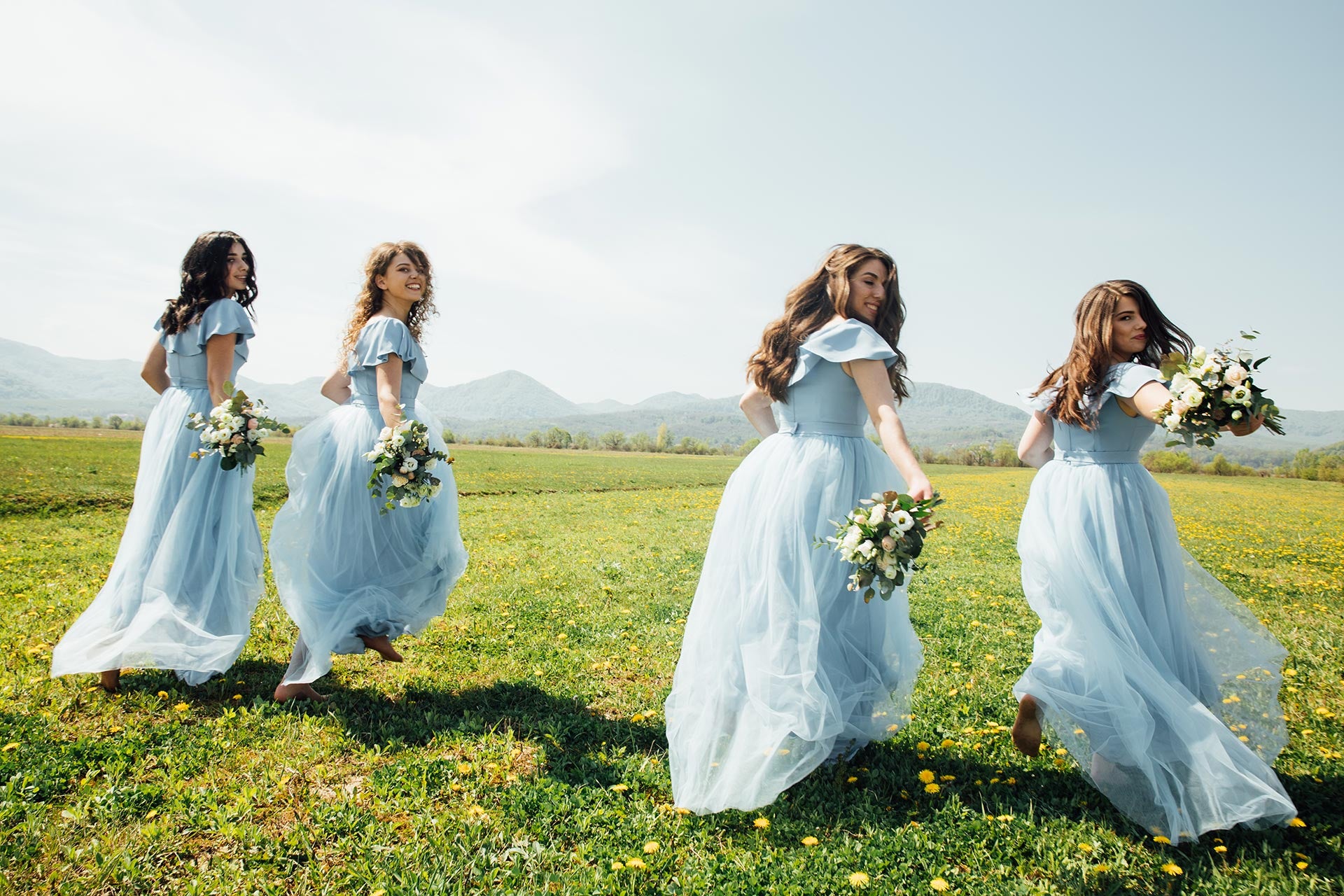 Pendamping pengantin dengan gaun biru dan buket bunga di padang rumput